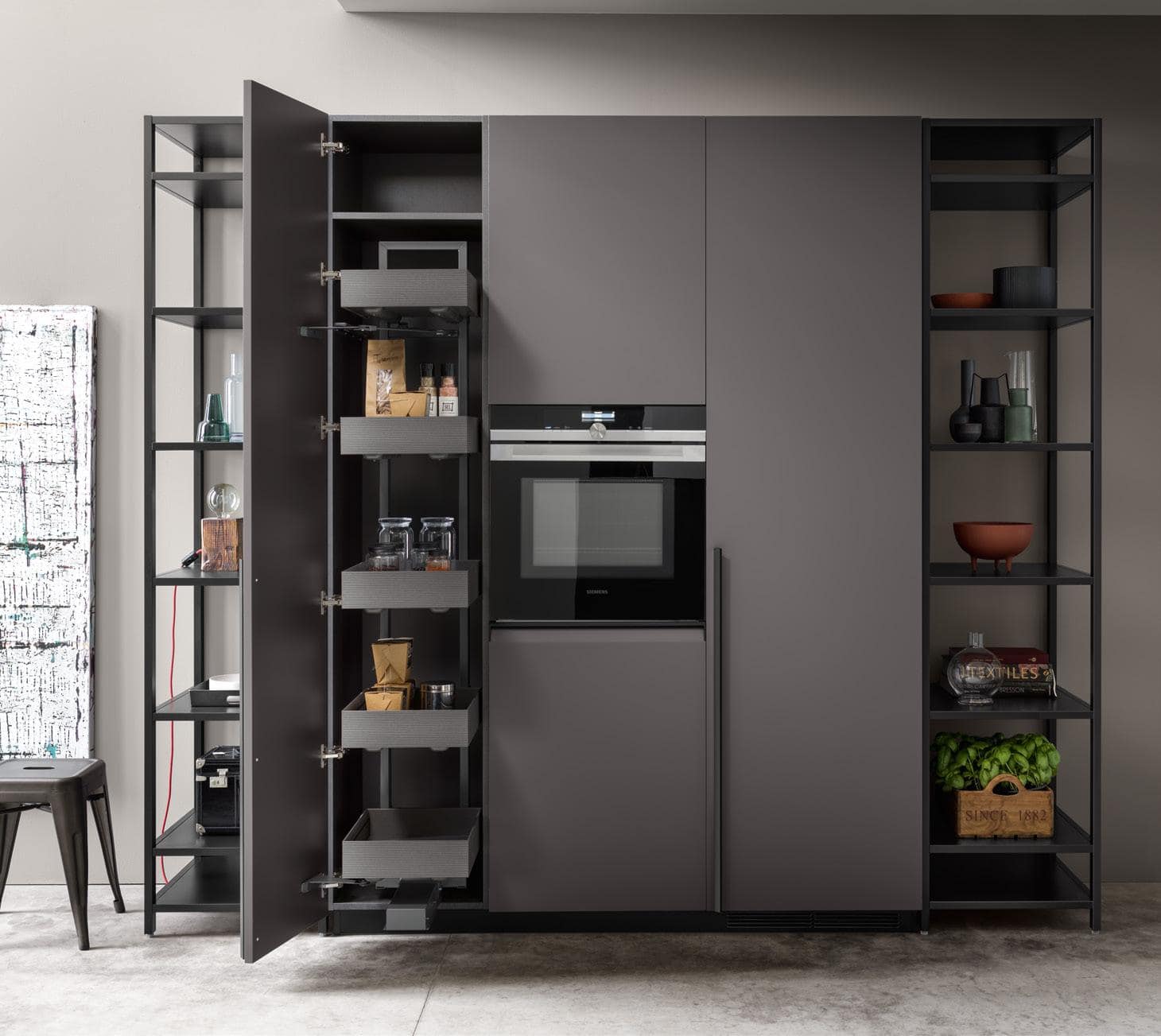 Modern kitchen cabinet with open pull-out shelves, built-in oven, and surrounding black shelving units displaying various items.