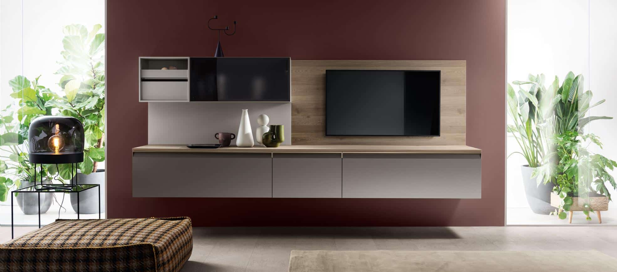 Modern living room with a wall-mounted TV, floating cabinets, decorative vases, and plants.