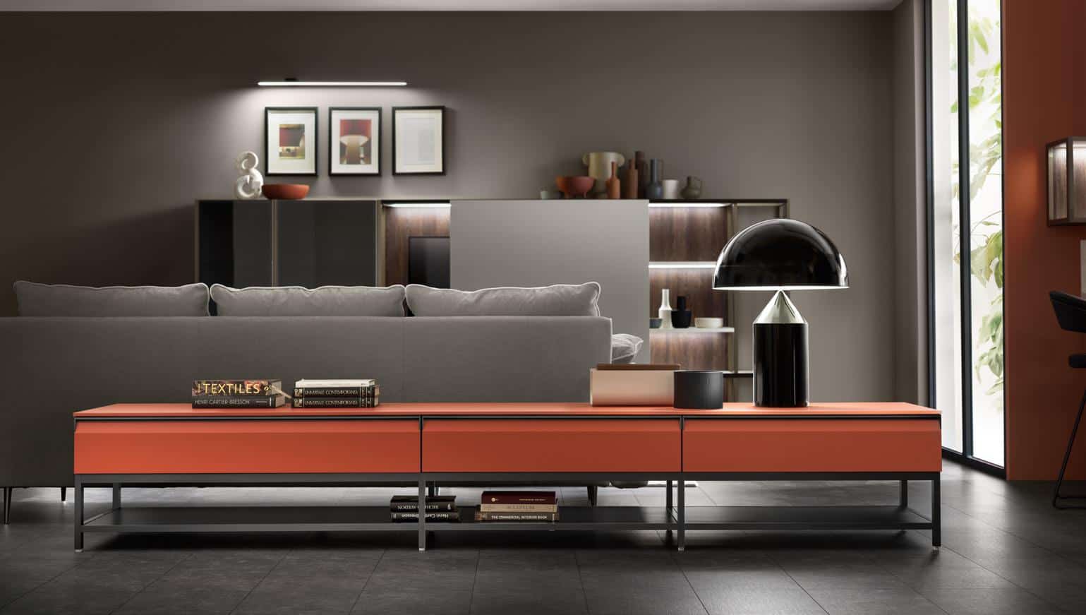 Modern living room with a gray sofa, orange console table, and a black lamp; artwork on the wall and shelves with decor items in the background.