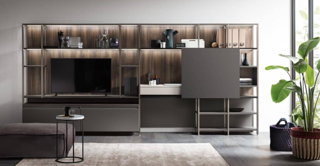 &quot;Modern living room interior with a wall-mounted entertainment center featuring a TV, shelves with decorative items, and storage cabinets, alongside a plant and a basket near a large window.&quot;