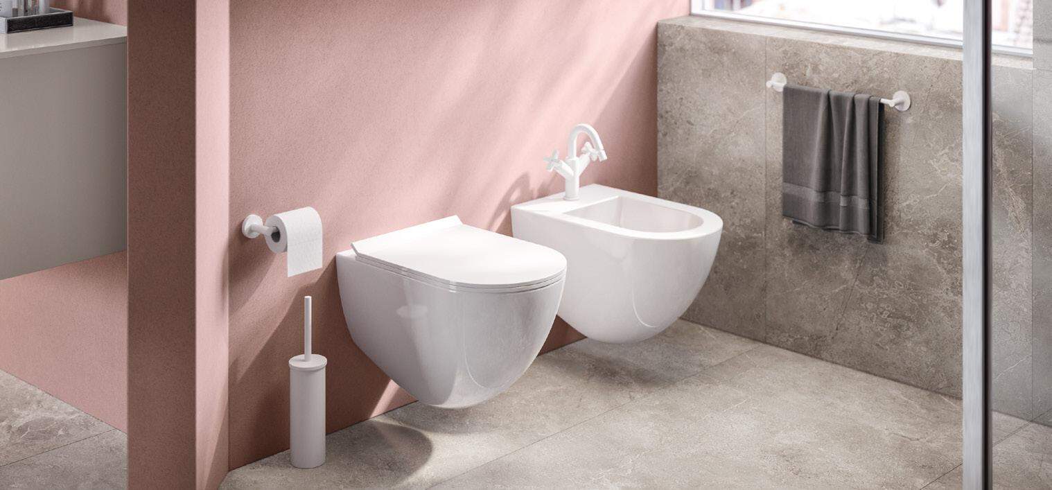 Modern bathroom with a wall-mounted toilet and bidet, pink walls, stone floor, and a towel rack.