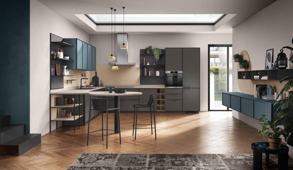 Modern kitchen with teal and gray cabinets, wooden herringbone floor, a central island with chairs, and pendant lights.
