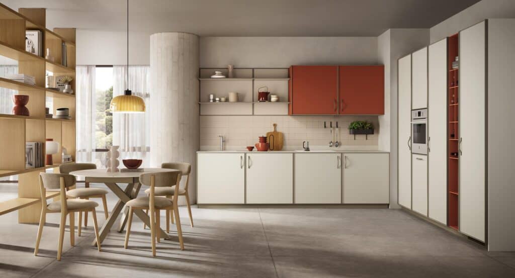 Modern kitchen with light-colored cabinetry, red accents, a circular dining table with four chairs, open shelving, and a pendant light, featuring a minimalist design and large windows.