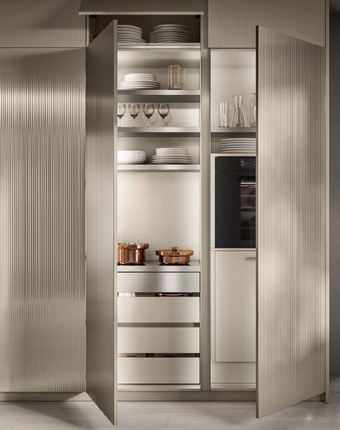 Interior of an open kitchen cabinet with shelves holding dishes, glasses, copper pots, and a built-in oven.