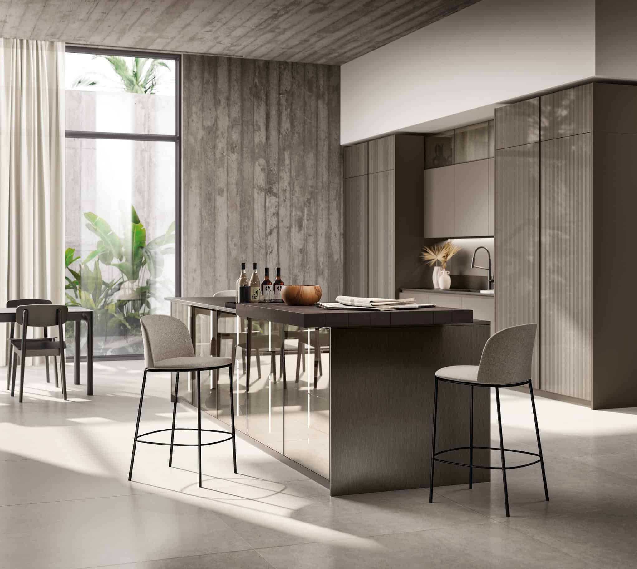 Modern kitchen interior with gray cabinetry, large island with bar stools, and a side table. Large window with plants visible outside, and natural light streaming in.