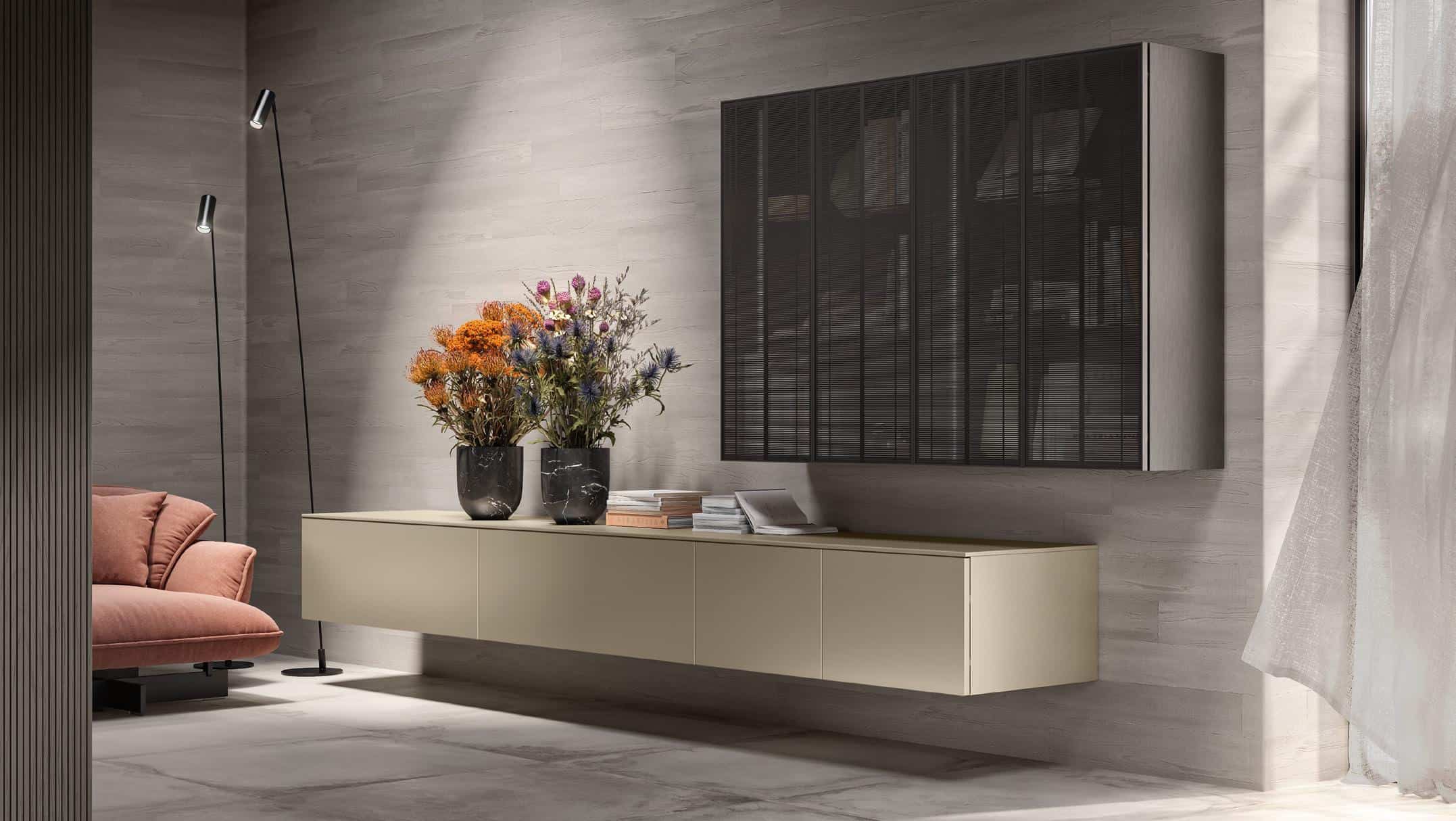 Contemporary living room with a wall-mounted beige cabinet, two black vases with colorful flowers, a sleek standing lamp, and a section of a pink sofa.