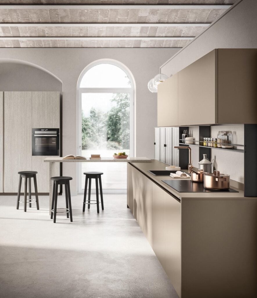 Modern kitchen with beige cabinetry, built-in oven, three black bar stools, and natural light from an arched window.