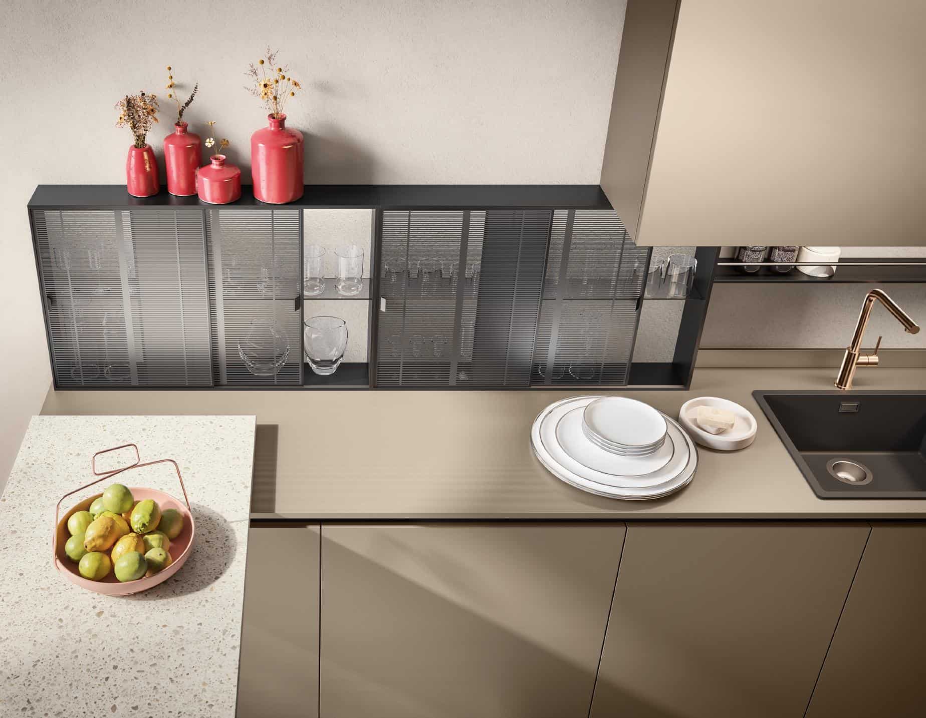 Modern kitchen countertop with a sink, gold faucet, stacked plates, decorative red vases with dried flowers, and a bowl of fruits.