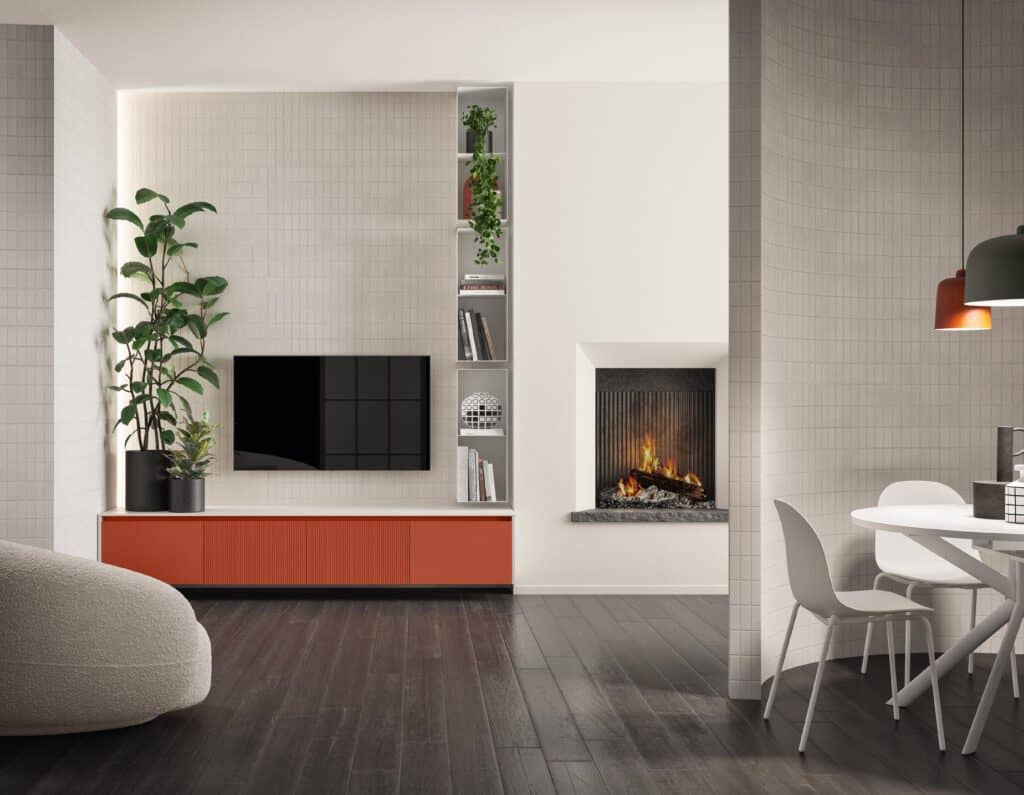 Modern living room with a flat-screen TV on the wall, orange low cabinet, large indoor plants, a fireplace with burning logs, a round dining table with white chairs, and white tiled walls.
