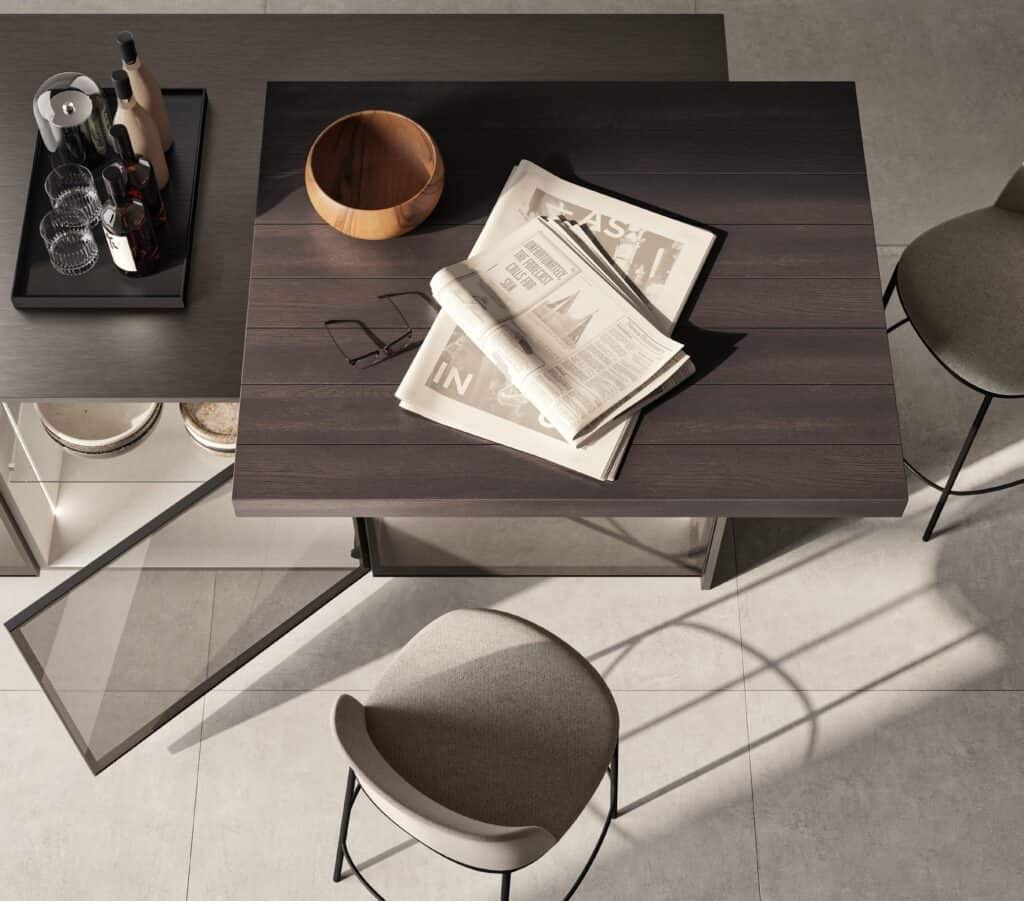 Modern kitchen island with a wooden top featuring a newspaper and glasses, surrounded by high chairs; a tray with bottles and glasses is on the side.
