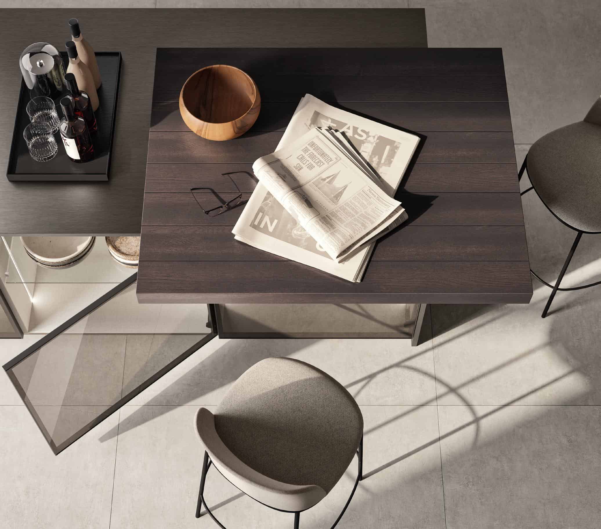 Modern kitchen island with a wooden top featuring a newspaper and glasses, surrounded by high chairs; a tray with bottles and glasses is on the side.