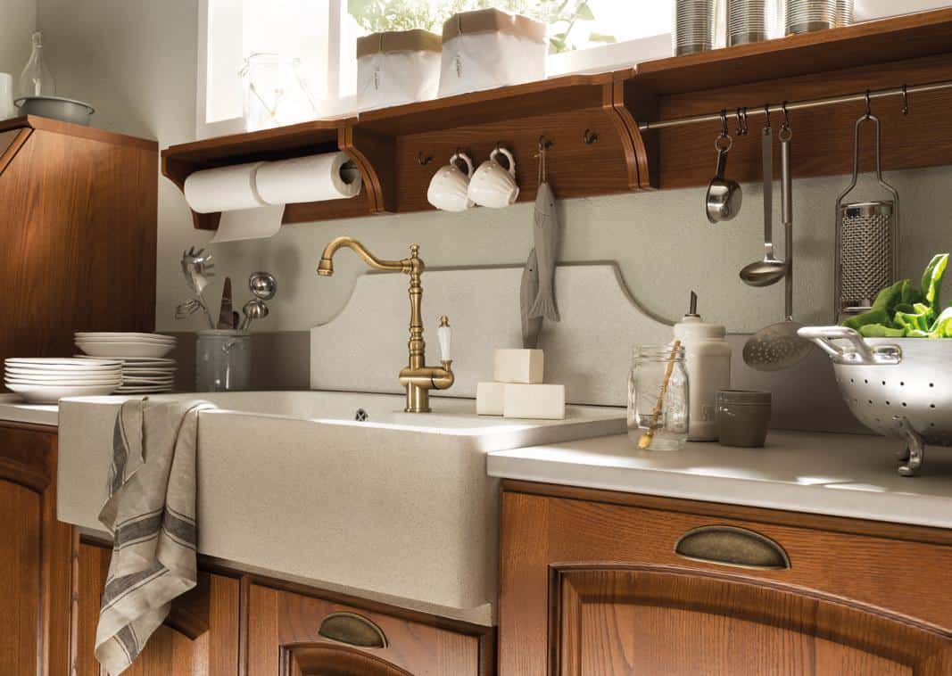 A rustic kitchen sink with a brass faucet, surrounded by wooden cabinets, dishware, and kitchen utensils.