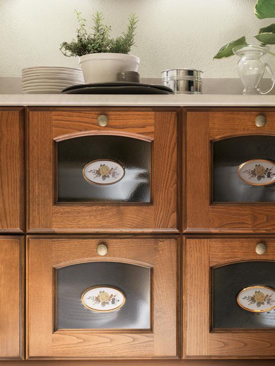 Wooden kitchen cabinets with black glass panels and floral designs, below a countertop with plants and dishes.