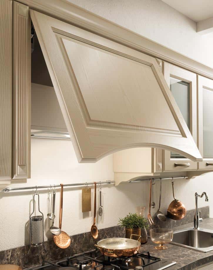 A modern kitchen with a raised wooden cabinet door, copper pots and utensils hanging on a rail, and a stainless steel sink.
