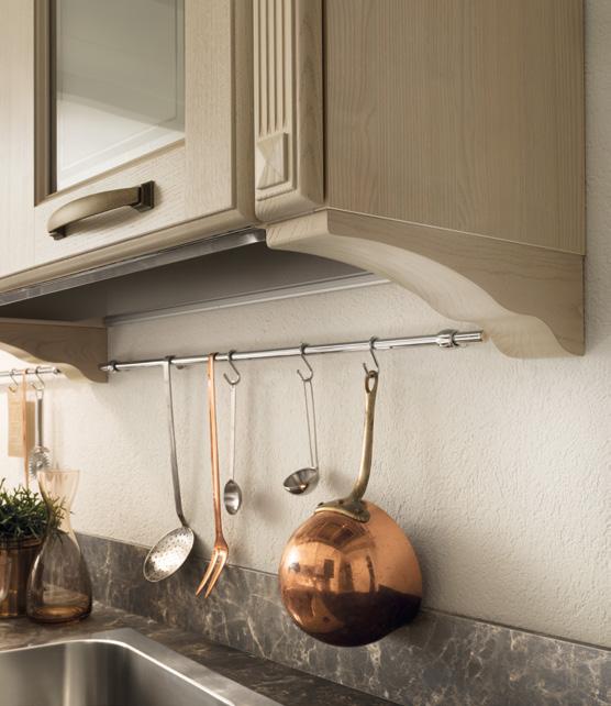 Kitchen utensils hanging on a metal rod under wooden cabinets, with a copper pot, ladle, slotted spoon, and fork above a marble countertop.