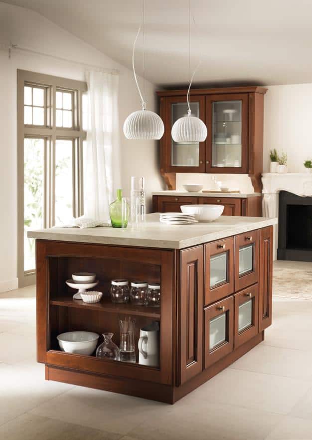 A modern kitchen with dark wood cabinets, a large island, glass-front drawers, white dishware, and pendant lighting.