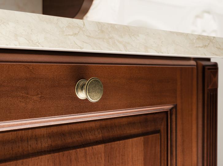 Wooden cabinet door with a round brass knob under a beige marble countertop.