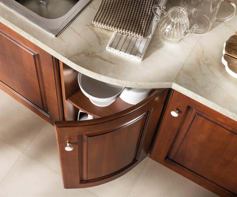 Wooden kitchen cabinet with curved shelves, displaying bowls under a marble countertop with various kitchen items.