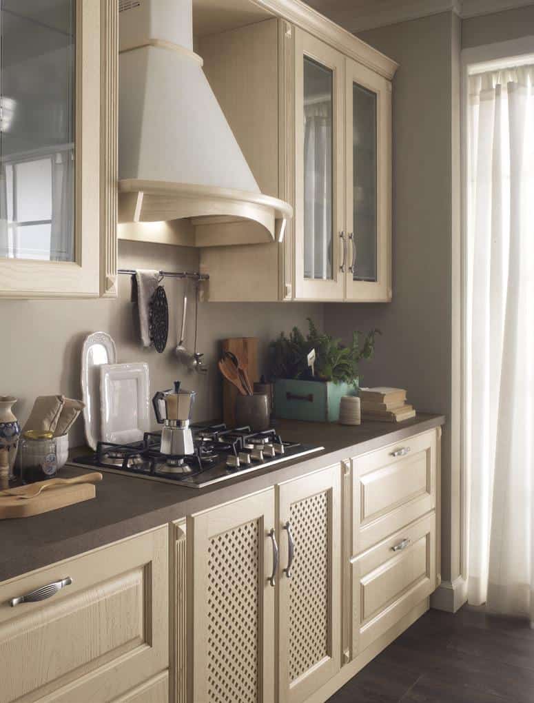 Traditional kitchen with light wood cabinetry, a range hood, countertop with a gas stove, utensils, and a moka pot.