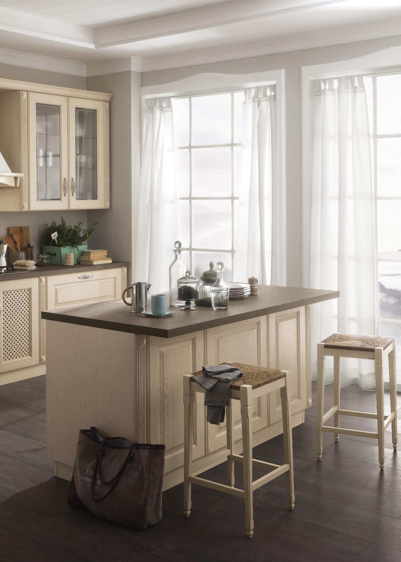 Cozy kitchen with beige cabinets, large windows with sheer curtains, and a central island with dark countertop and rustic stools.