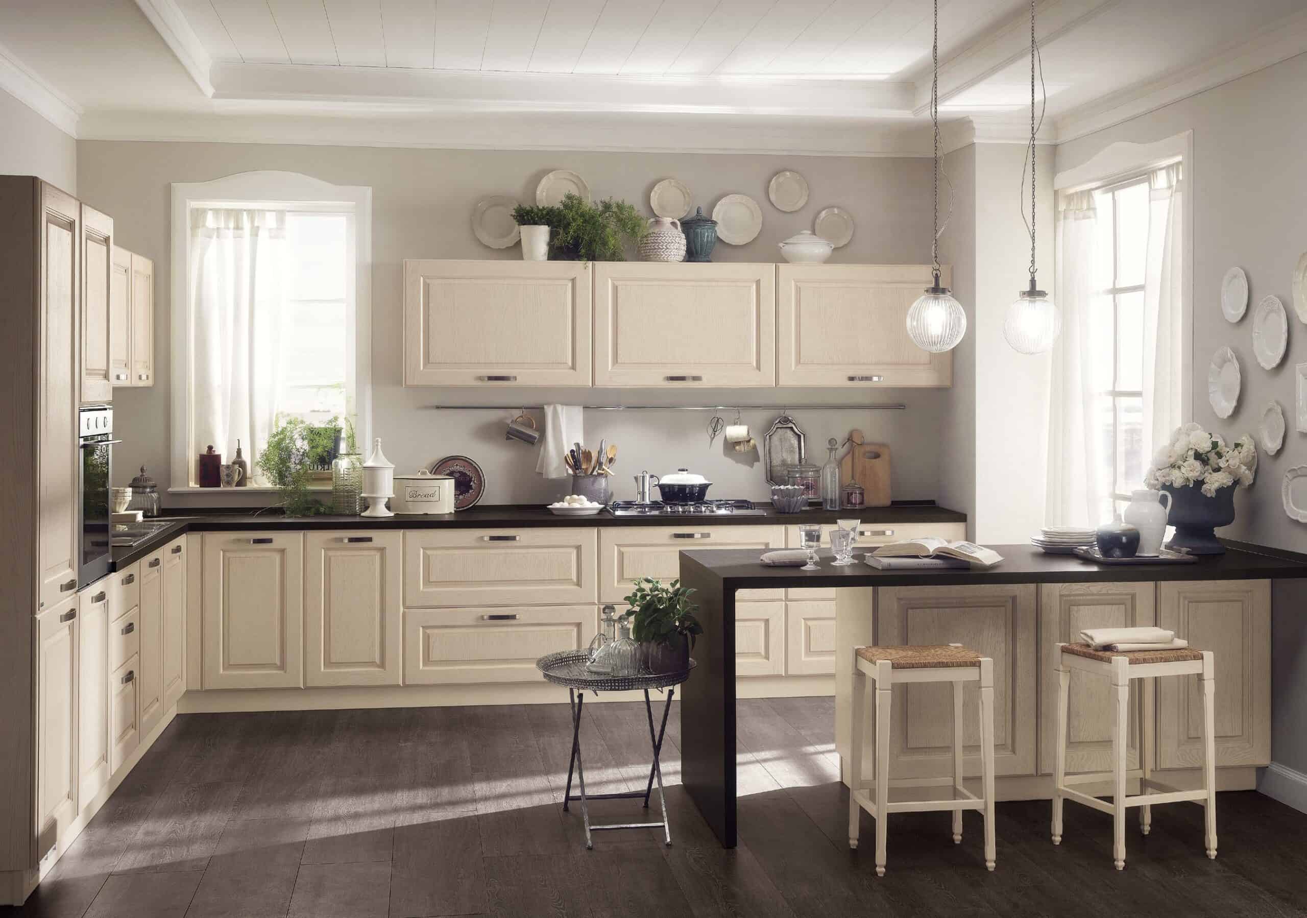 A cozy kitchen with cream-colored cabinets, dark countertops, pendant lighting, and a small breakfast bar with stools.
