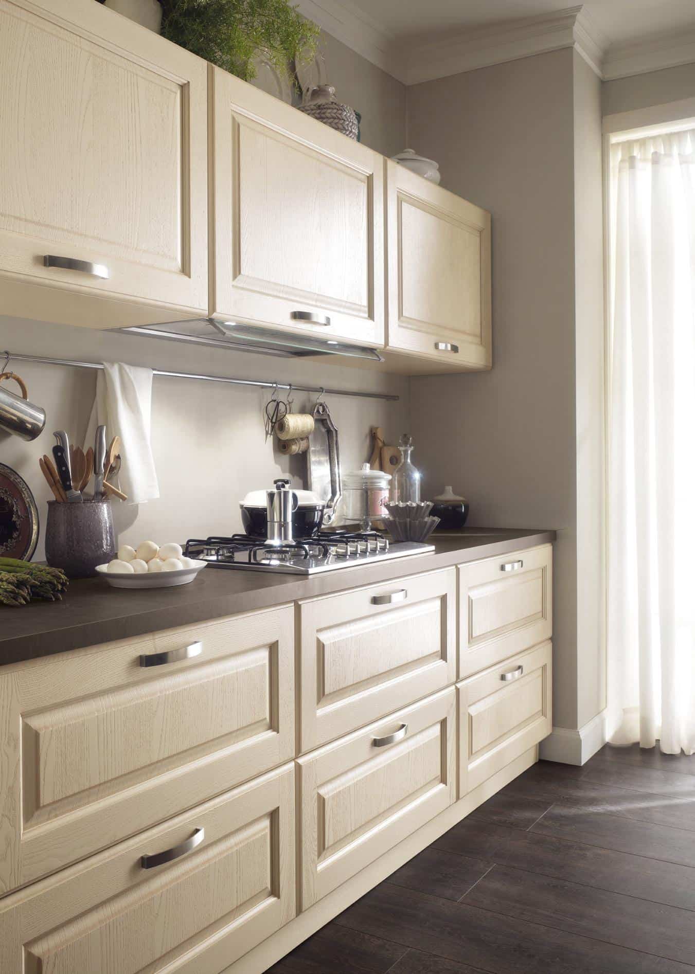 Beige kitchen with wooden cabinets, a dark countertop, a gas stove, and kitchen utensils.
