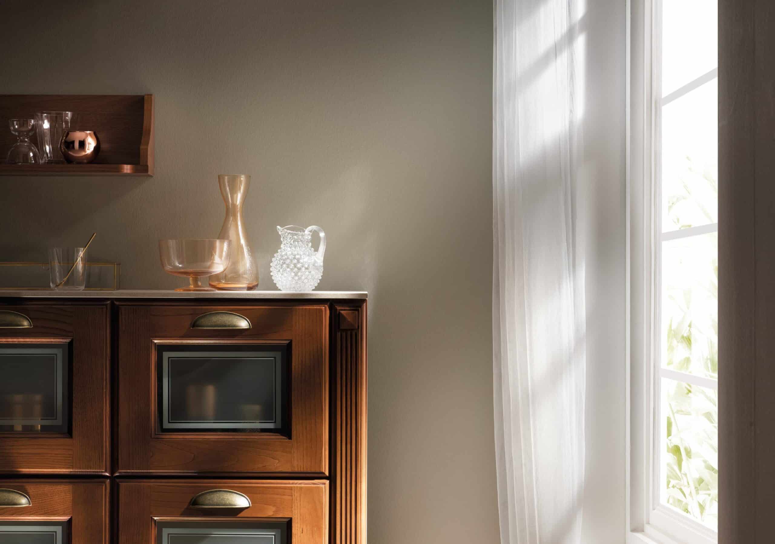 Cabinet with glassware and ceramics, next to a window with sheer curtains.