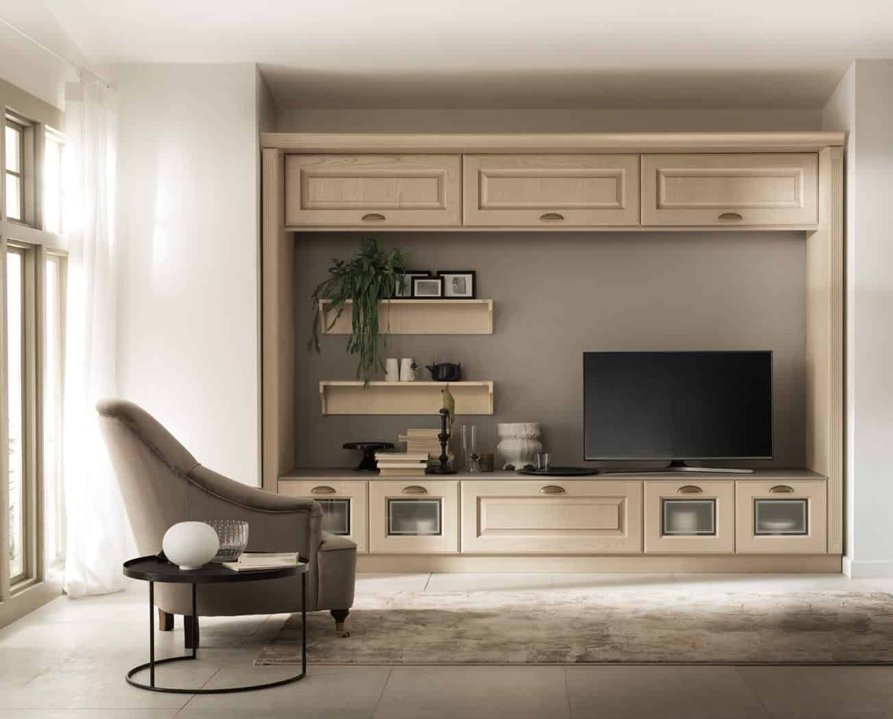Living room featuring a wall-mounted wooden entertainment unit with a TV, shelves, potted plant, and decorative items, alongside an upholstered armchair and round side table near a window.