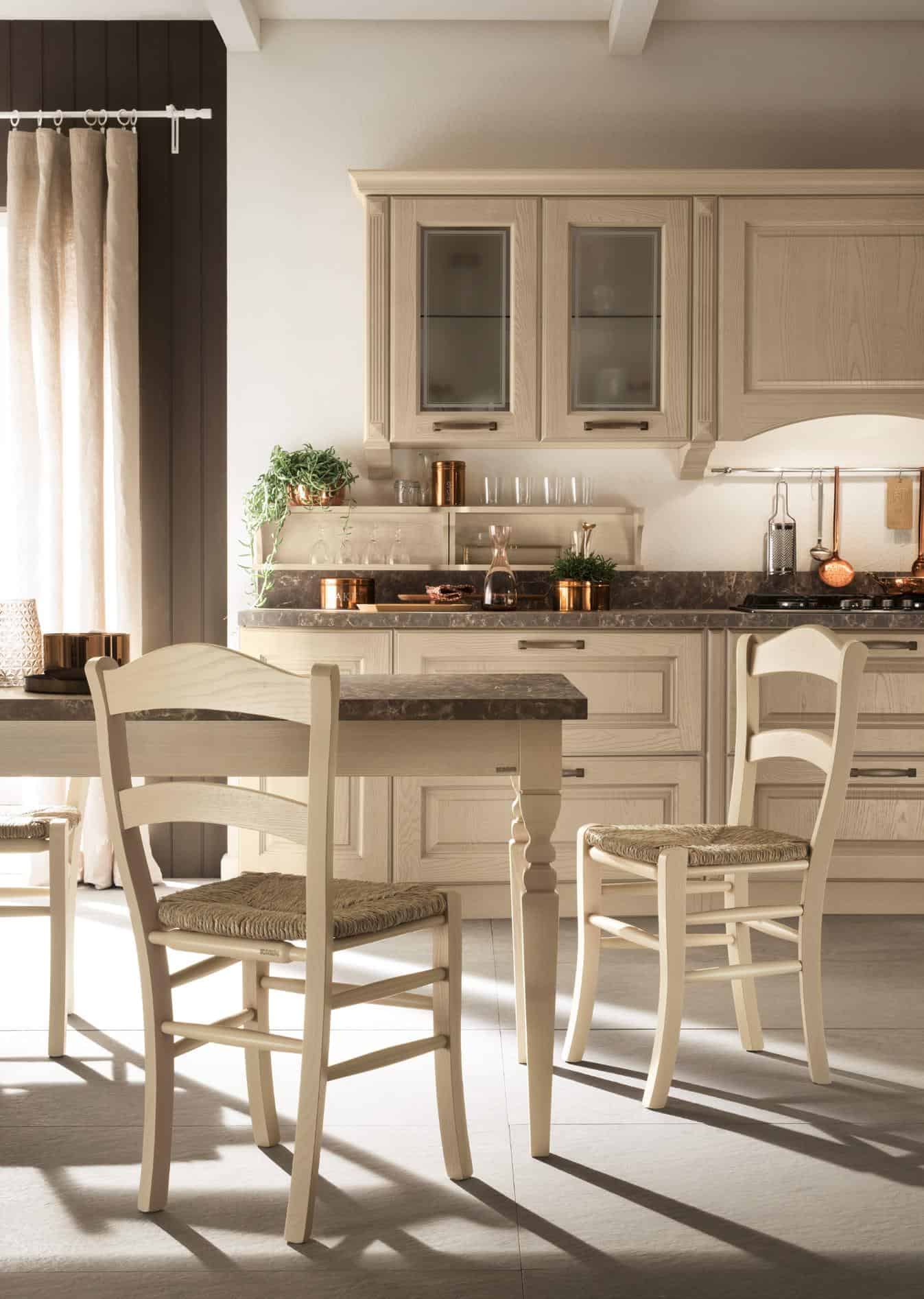 Cozy kitchen with wooden furniture, light-colored cabinets, table with wicker chairs, and decorative plants on the counter.