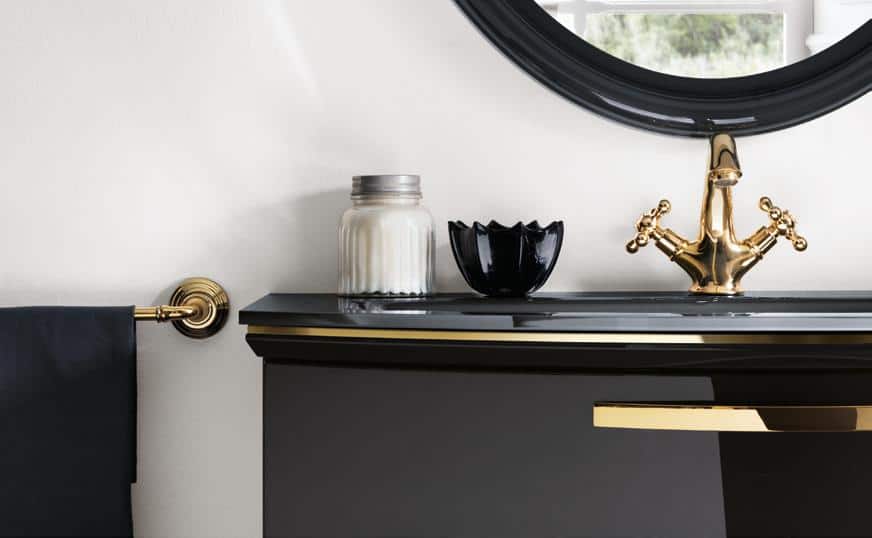 Bathroom sink with a gold faucet, black countertop, and decorative items including a black bowl and a glass jar.
