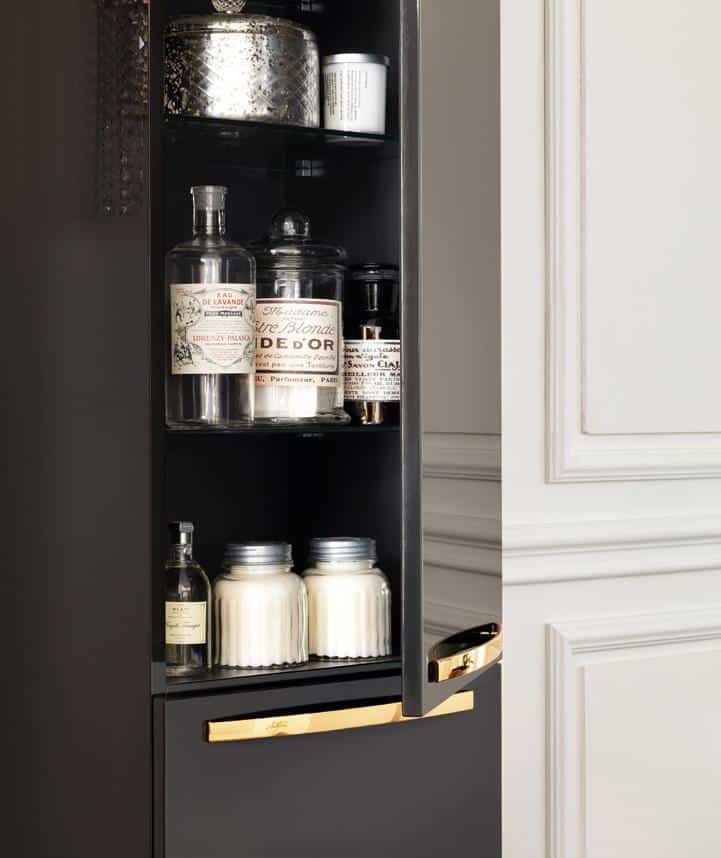 Cabinet with glass jars and bottles on shelves, featuring gold-accented handles.