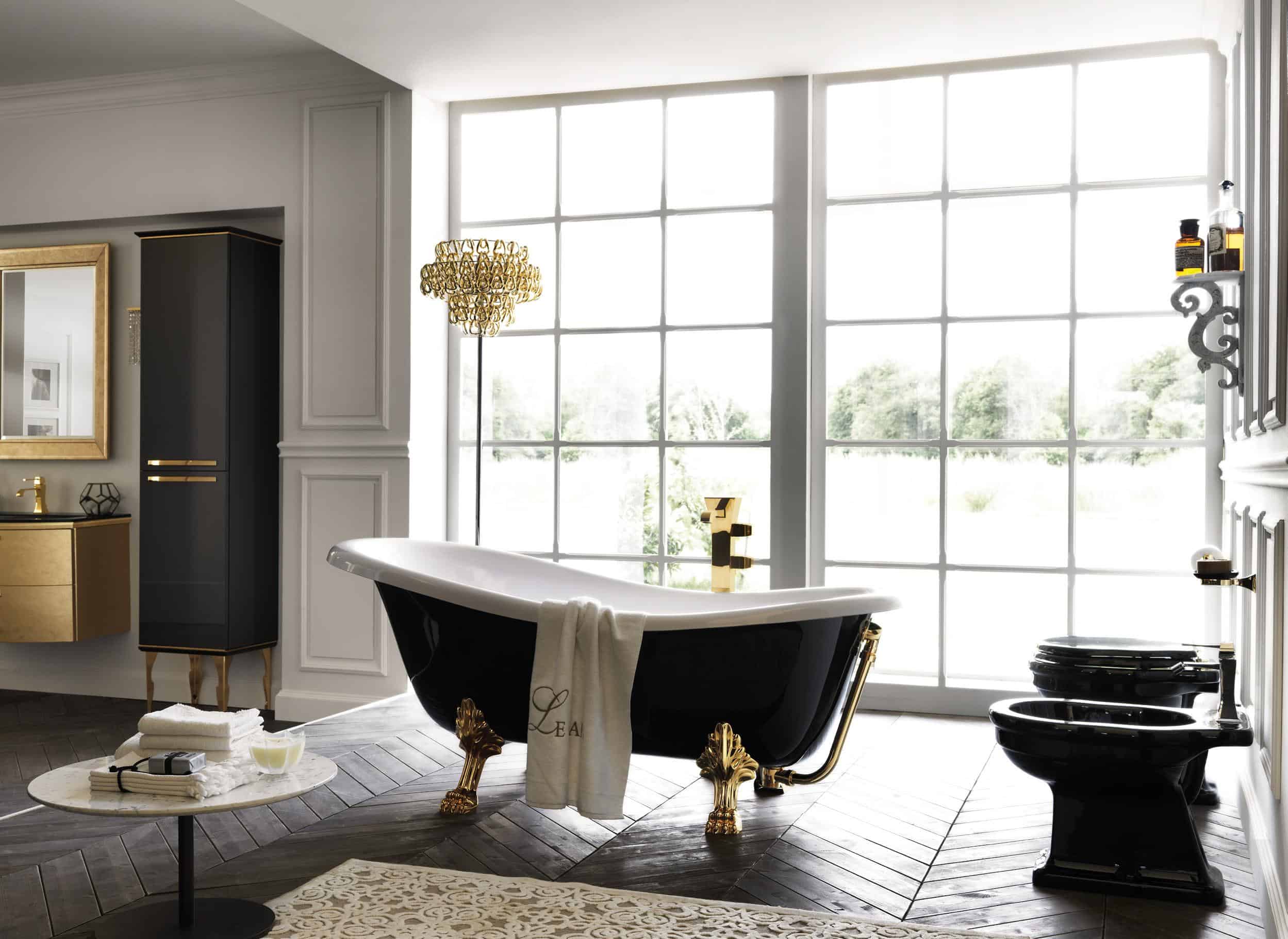 Elegant bathroom with a black clawfoot bathtub, gold fixtures, large windows, and a decorative chandelier.