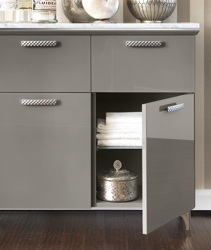 A gray cabinet with textured metal handles, one door open revealing folded towels and a decorative silver container inside.