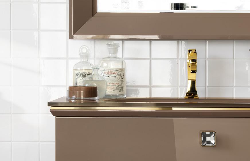 A bathroom vanity with a reflective gold faucet, brown drawer, crystal knob, and glass bottles.