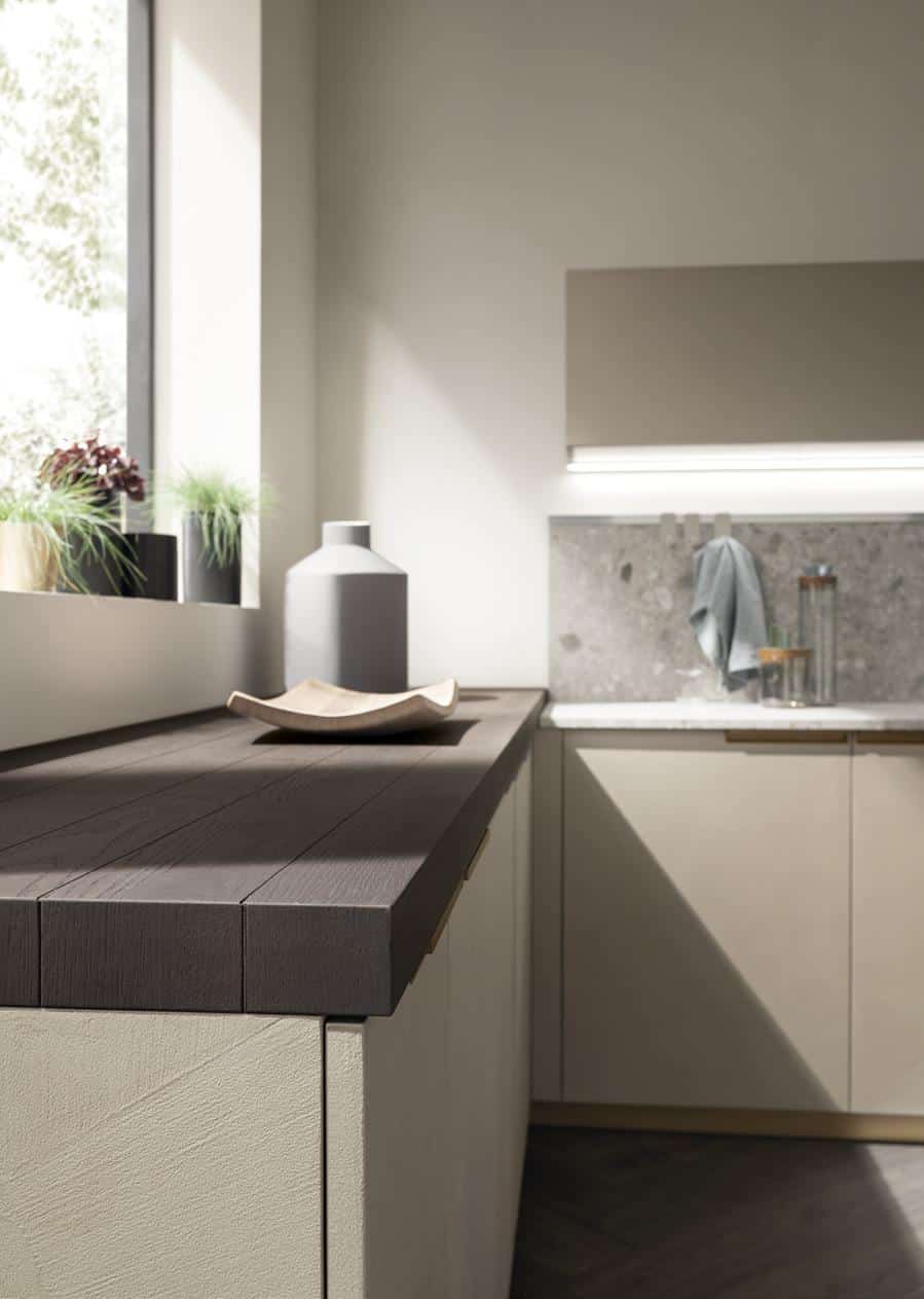 Modern kitchen interior with wood countertop, plants on the windowsill, and gray cabinets.