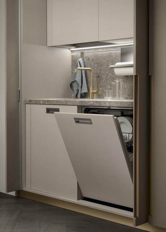 Open modern kitchen dishwasher with beige cabinetry and marble countertop, brass faucet, and dishrack visible.