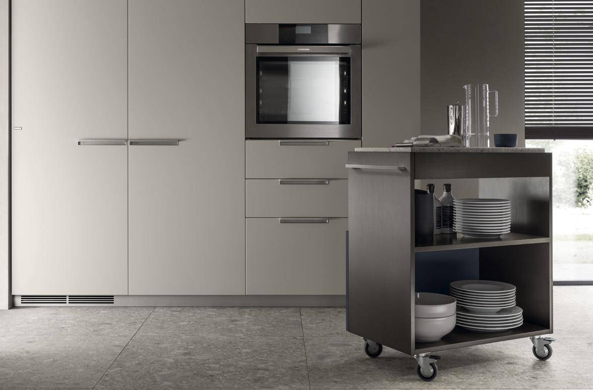 Modern kitchen with integrated oven, minimalist cabinets, and a mobile cart with shelves holding dishes and bottles.