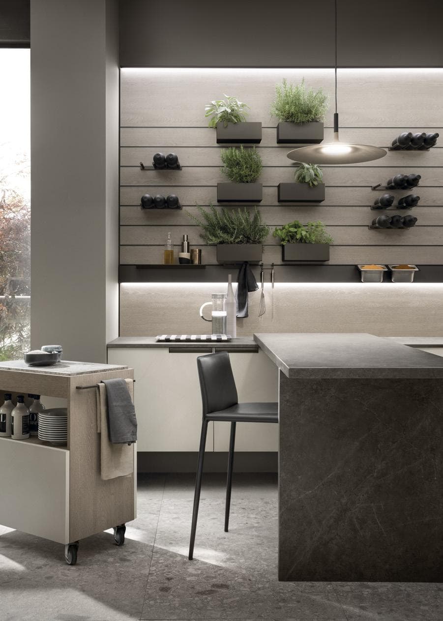 Modern kitchen with a dark stone island, black chair, wall-mounted plant holders, wine racks, and a pendant light.