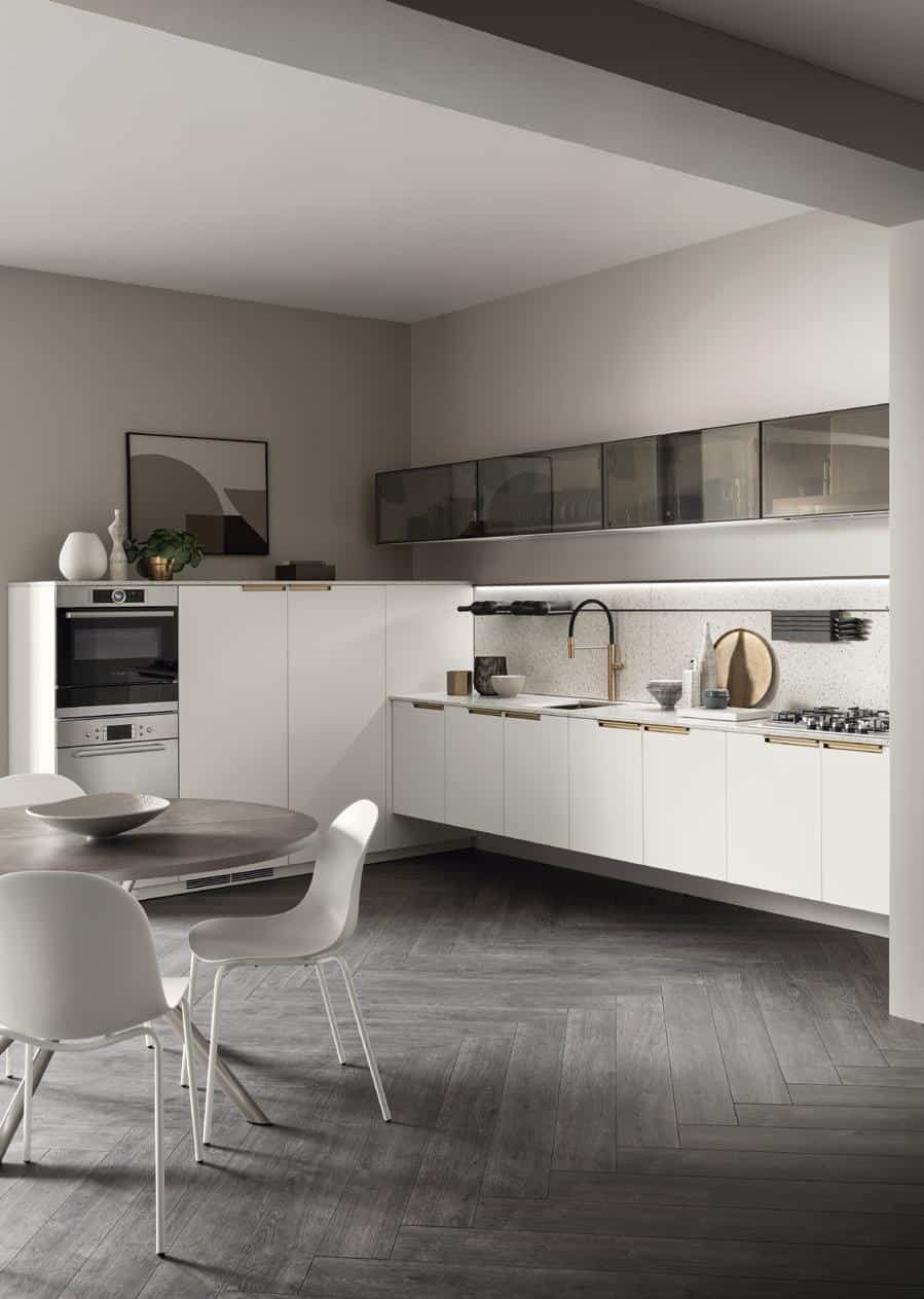 Modern kitchen with white cabinets, black countertop, integrated appliances, and gray herringbone floor, featuring a round dining table with white chairs.