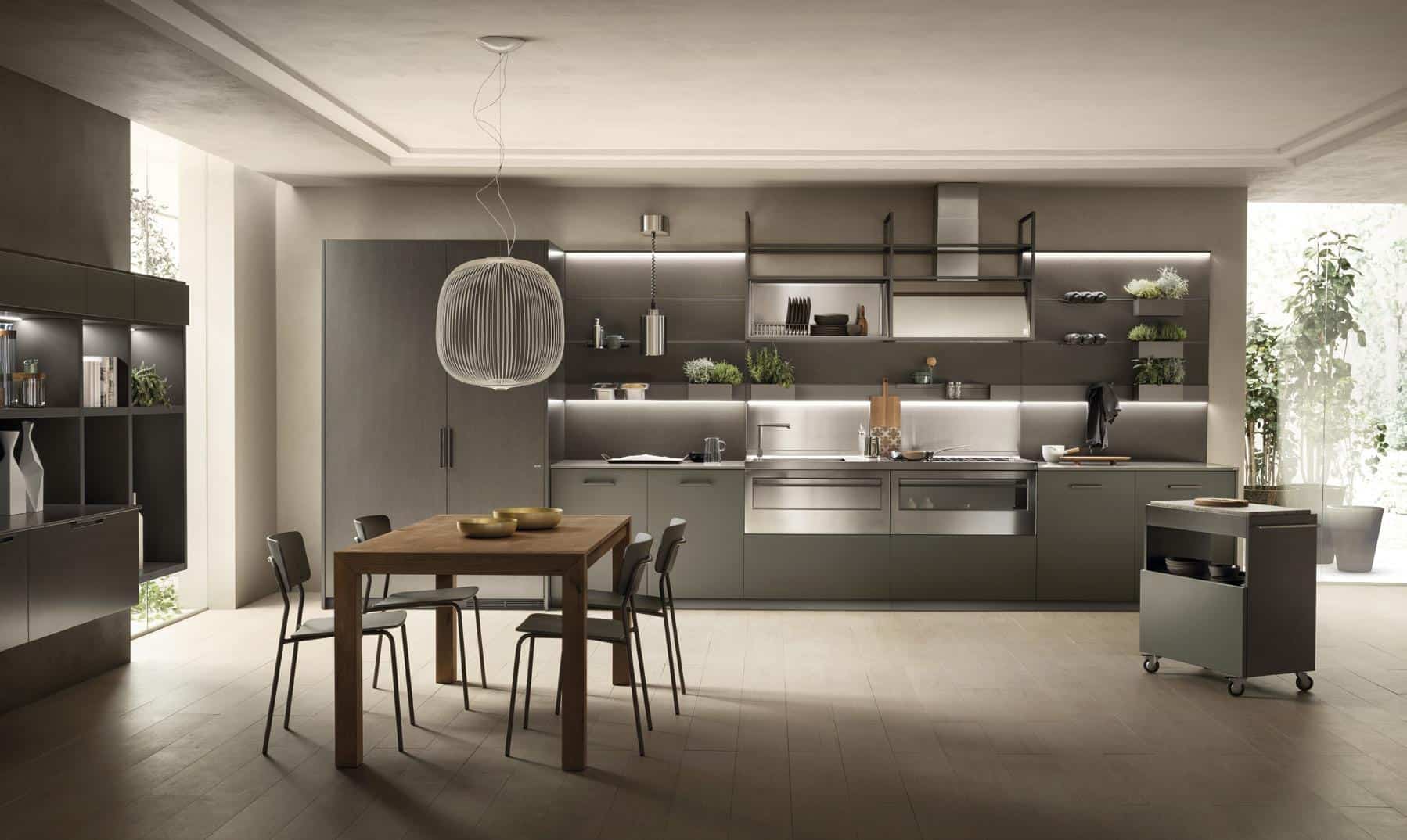 Modern kitchen interior with grey cabinetry, stainless steel appliances, a wooden dining table with four chairs, and a pendant light above.