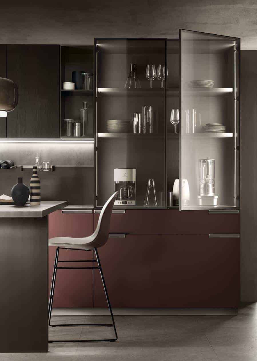 Modern kitchen interior with dark cabinetry, glass-fronted cabinets, a kitchen counter, and a high chair.