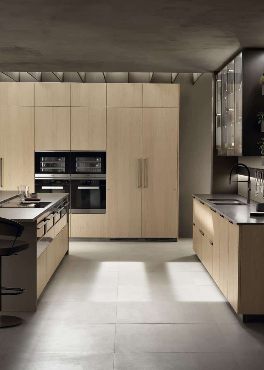 Modern kitchen with light wood cabinetry, built-in ovens, and a sleek island with bar seating.