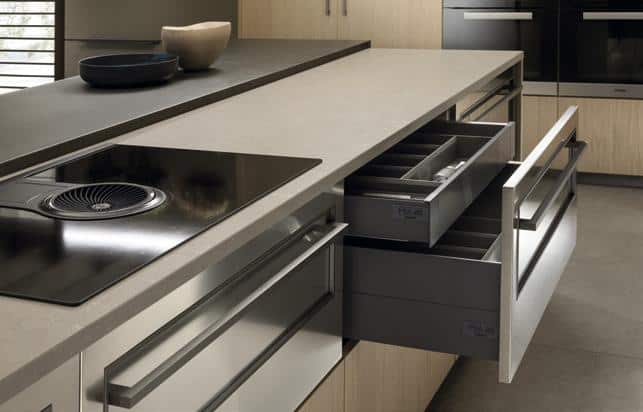 Modern kitchen with grey countertop, induction stovetop, and open stainless steel drawers.