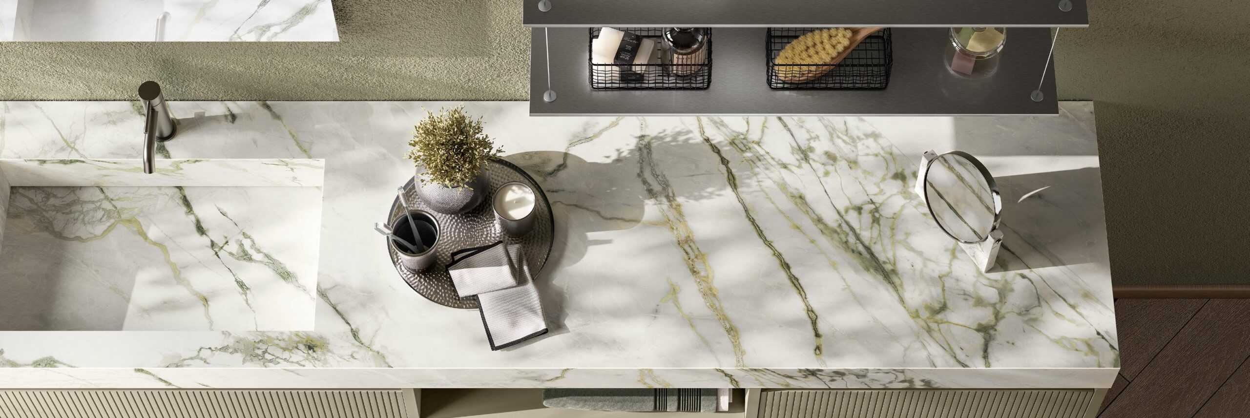Marble countertop with a modern sink, faucet, a round tray holding a potted plant, cup, candle, and cloth, with a shelf above.
