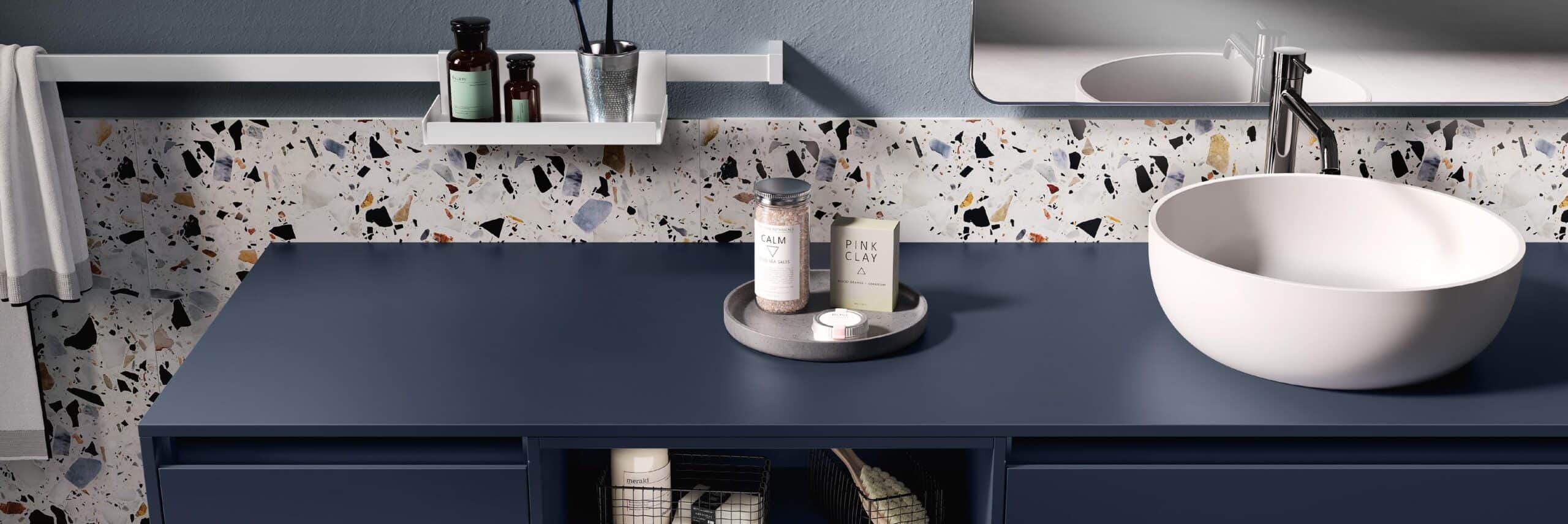 Modern bathroom vanity with dark blue countertop, round white basin, terrazzo backsplash, and cosmetics displayed on the counter.