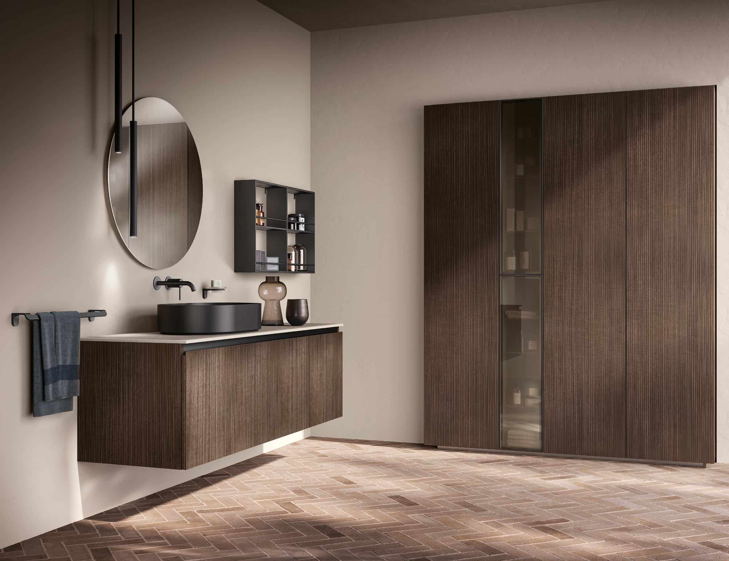Modern bathroom with a round mirror, dark basin, wooden cabinetry, and a towel rack against a neutral-colored wall.