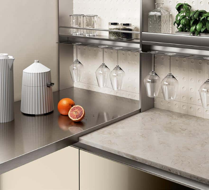 Modern kitchen counter with a stainless steel surface, a citrus juicer, a sliced blood orange, hanging wine glasses, a basil plant, and shelves with glass containers and spice jars.
