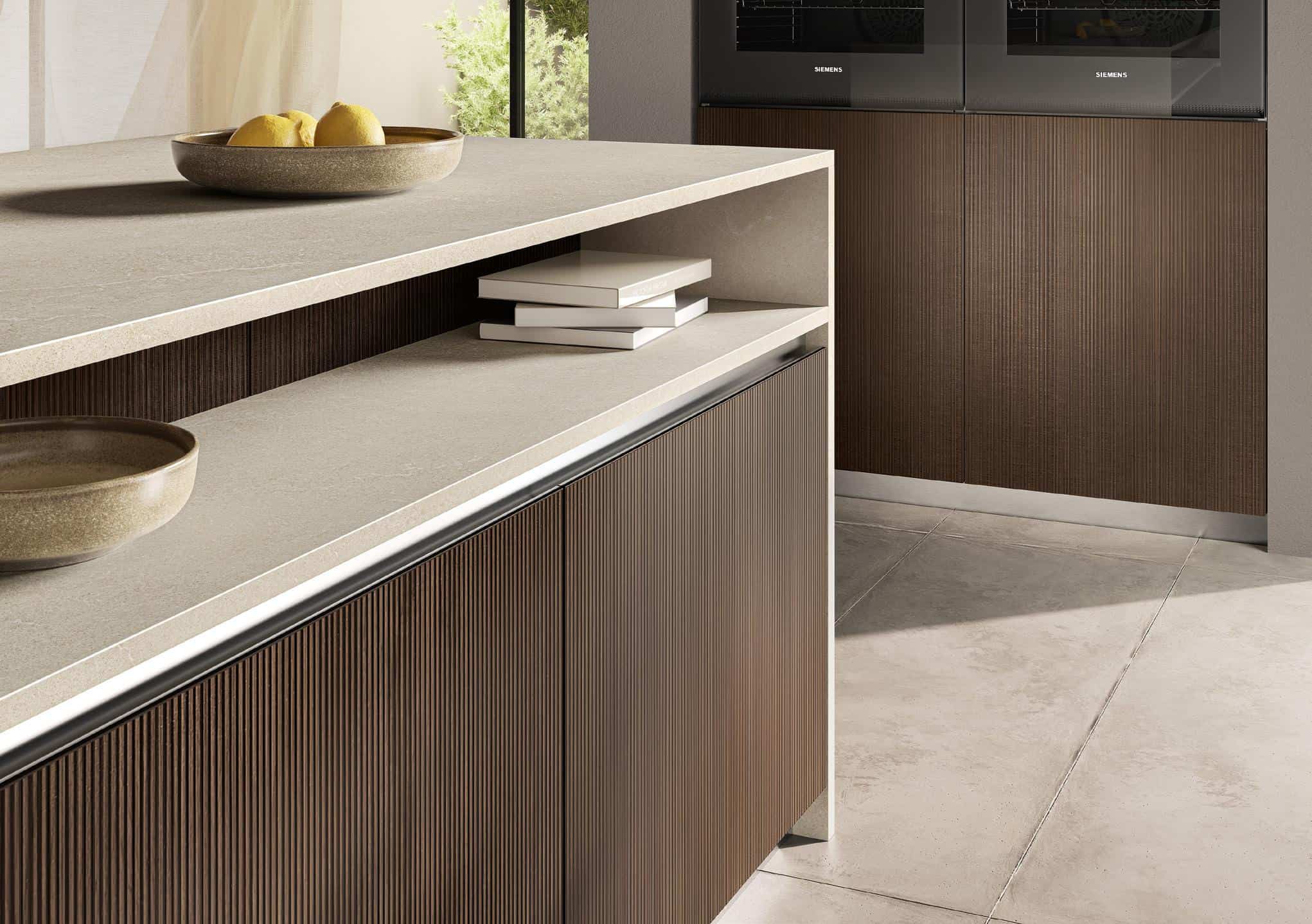 Modern kitchen with brown cabinetry, light stone countertops, a bowl of lemons, and stacked books.