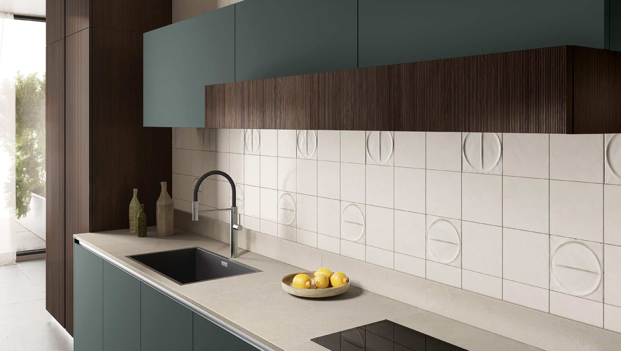 Modern kitchen with teal cabinets, a dark faucet over a black sink, light countertops, patterned white backsplash tiles, and a bowl of lemons.