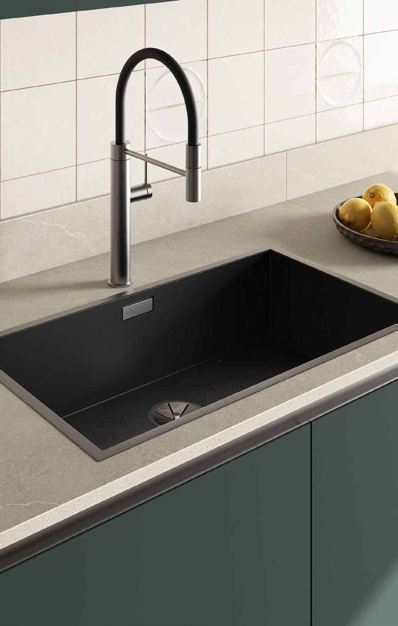 A modern kitchen sink with a black basin and a sleek, high-arc metallic faucet, set in a light countertop with green cabinetry. A bowl of lemons is on the counter.